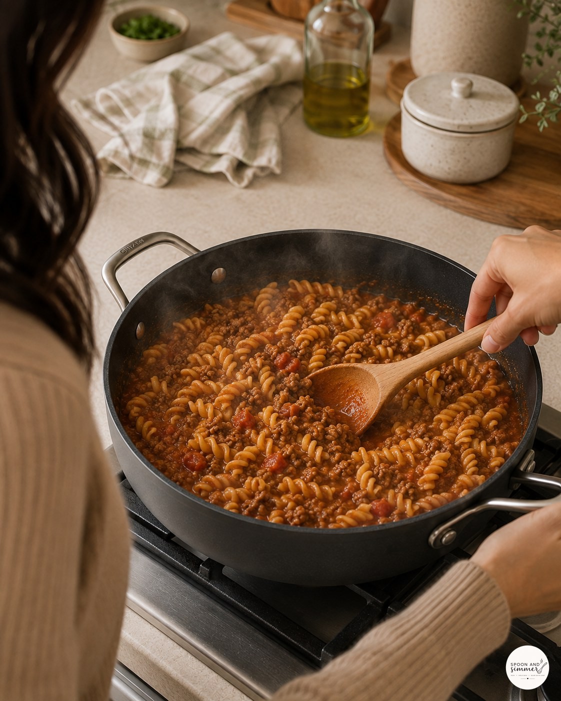 Stirring rotini pasta simmering in tomato beef sauce in a large skillet