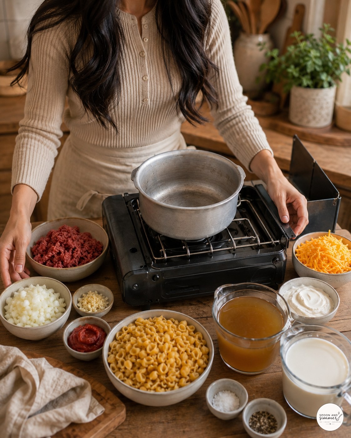 Cook standing at a wooden table with a camp stove and ingredients arranged for hamburger helper