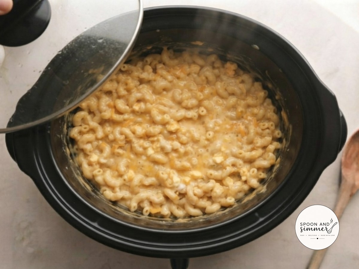 The lifted lid reveals softened pasta in a glossy, nearly melted cheese sauce underneath.